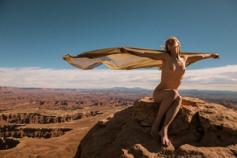A nude woman opens her arms in flight in Canyonlands National Park