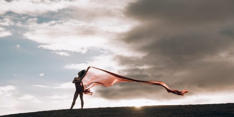A partially nude woman dances with long read fabric during sunrise