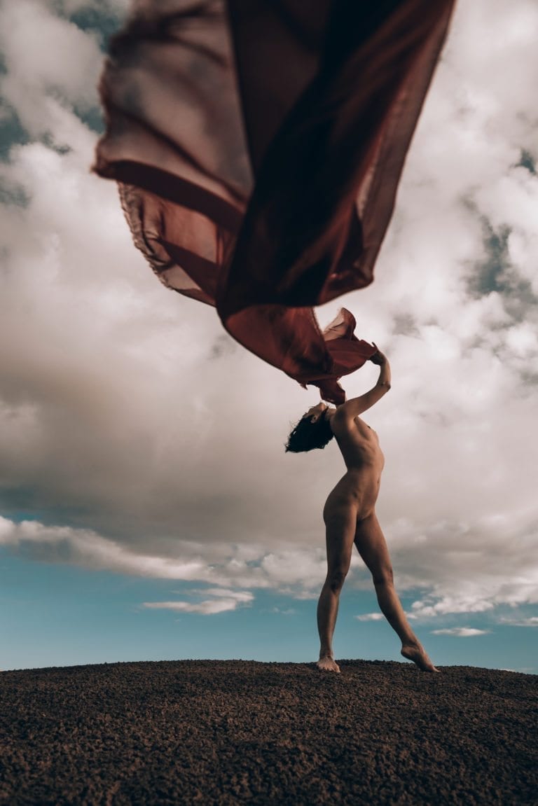 A nude woman dances with red fabric in the desert