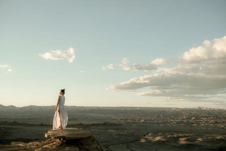 A woman in a white dress looks over a vast desert landscape