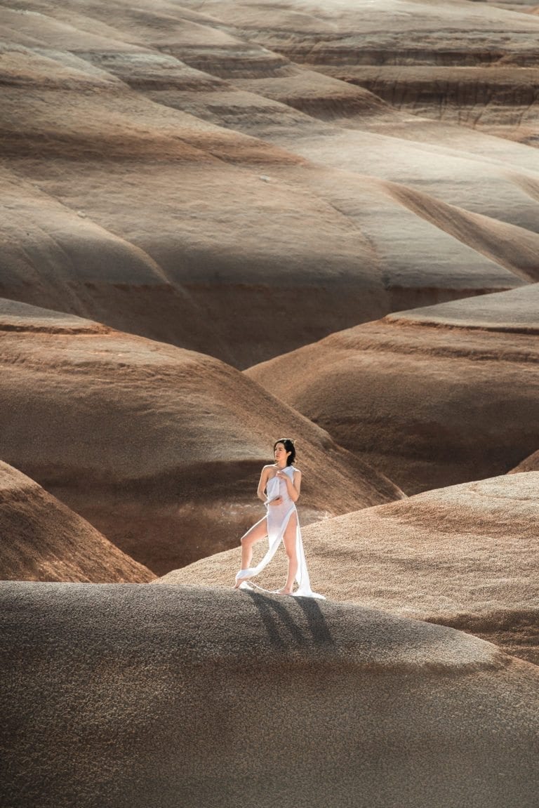 A woman in a white dress poses in sand dunes