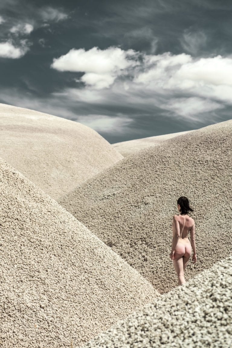 A black haired woman walks through desolate sand dunes
