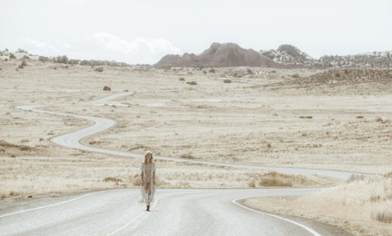 A woman walks partially nude on a winding desert road