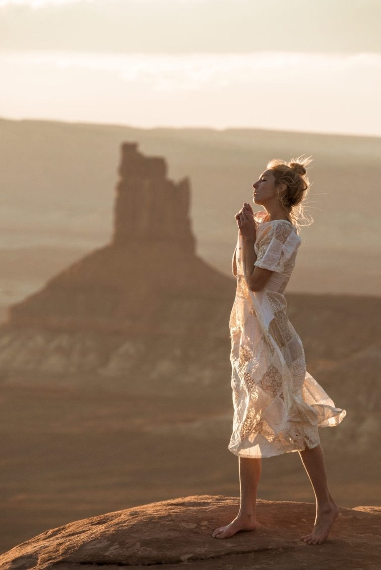 A woman pulls her dress up in front of a butte in the Utah desert