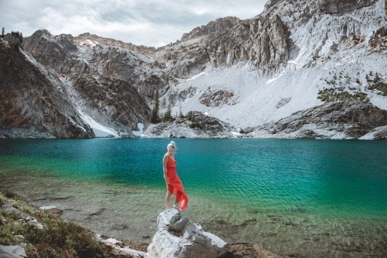 A woman in a red dress poses in front of a high-alpine lake