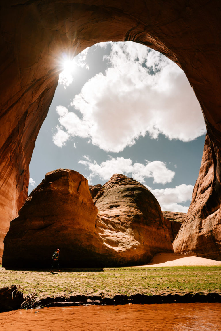 A woman walks under massive alcove in Davis Gulch.
