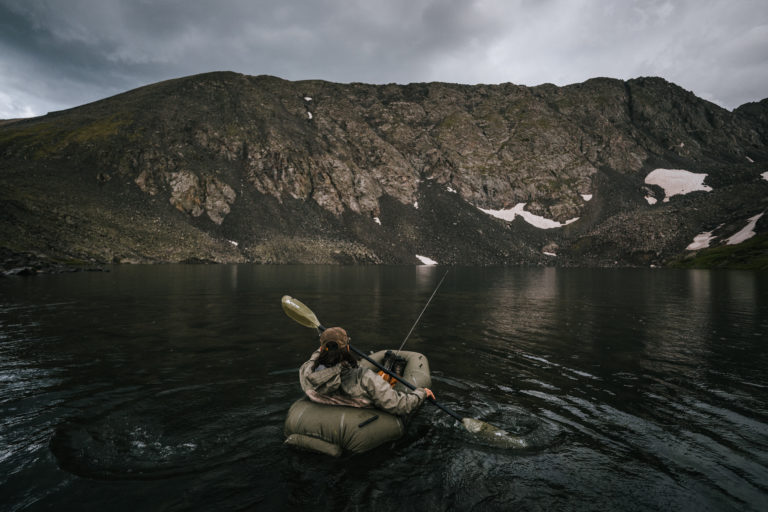 A man paddles out into a high alpine lake right before a rain storm.