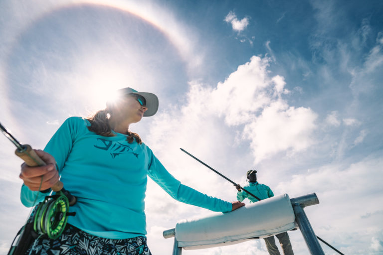 A woman looks for bonefish with a Sundog behind her