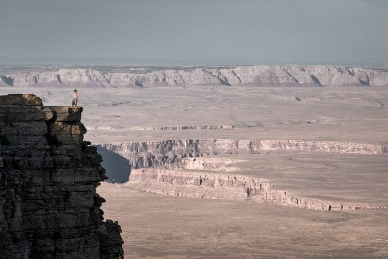A woman in a dress stands on the edge of a cliff, overlooking Marble Canyon and the Vermillion Cliffs in northern Arizona.