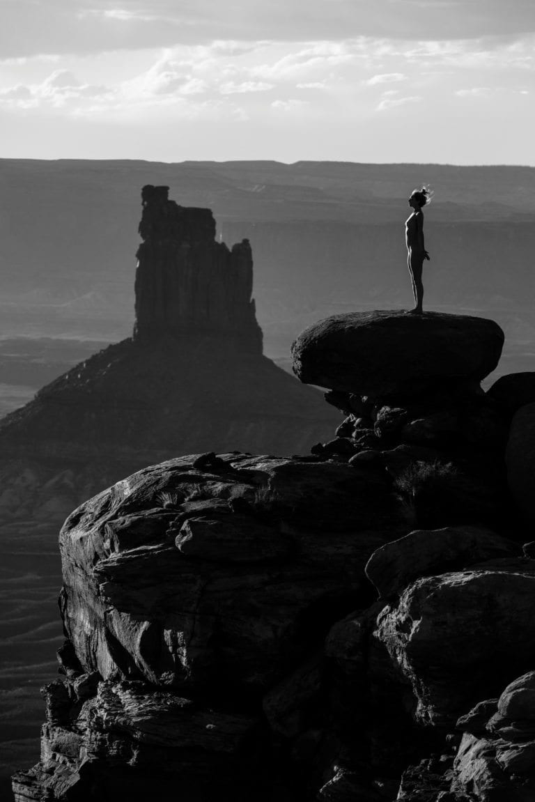 A nude woman stands tall in front of a large butte in southern Utah