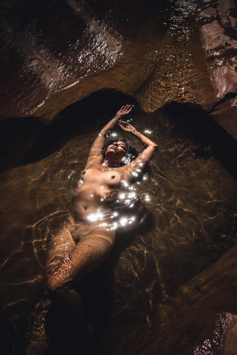 A woman floats nude in the water of a  slot canyon