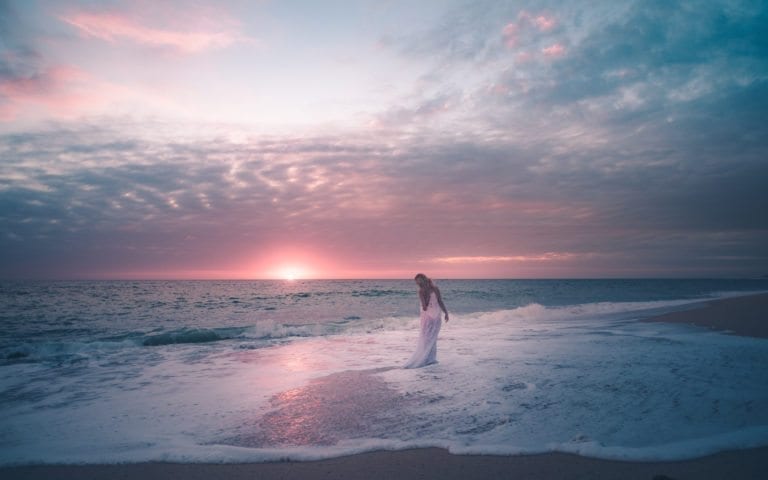 Woman in a white dress dances in the ocean during sunset