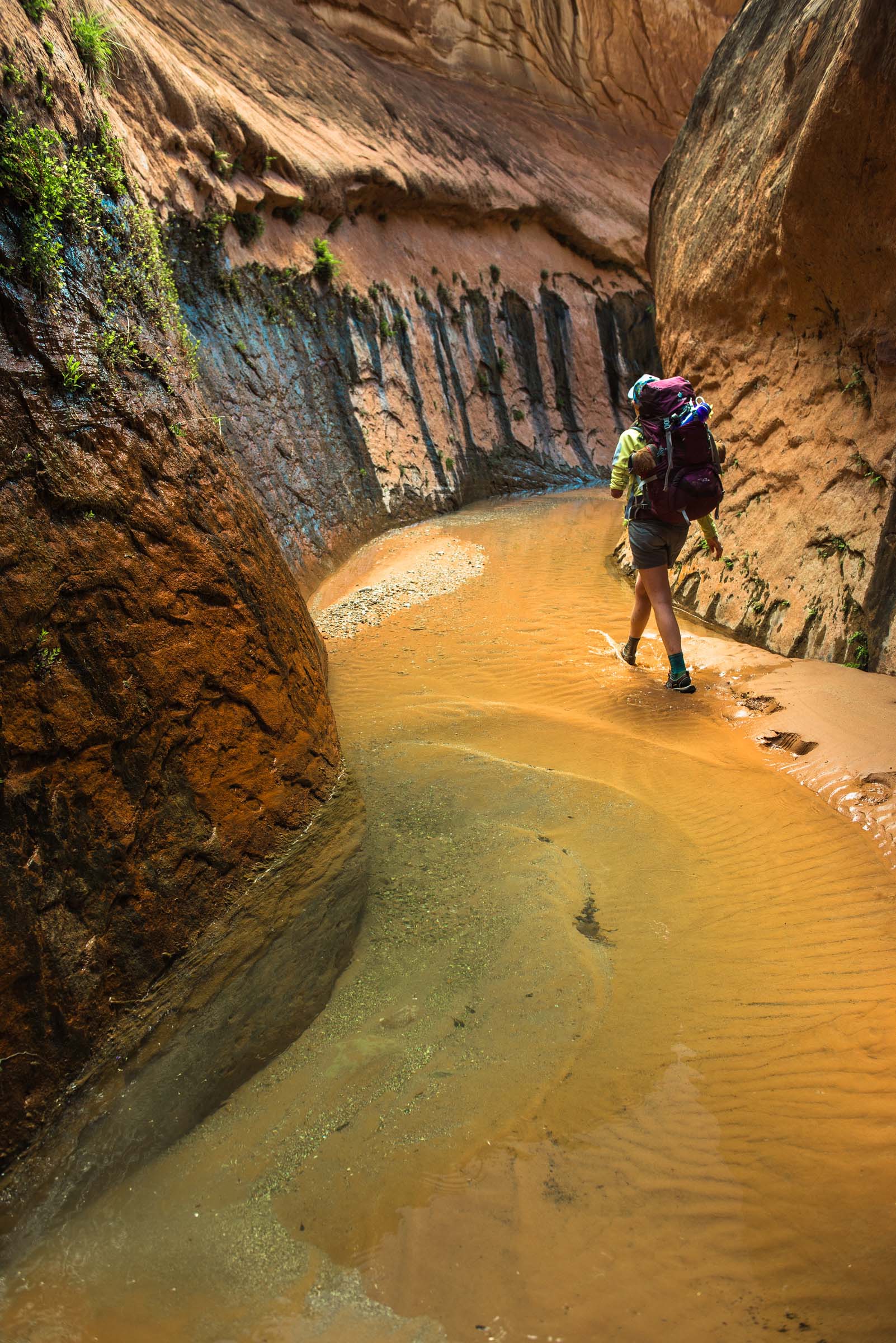 A woman backpacker walks through a very colorful slot canyon.