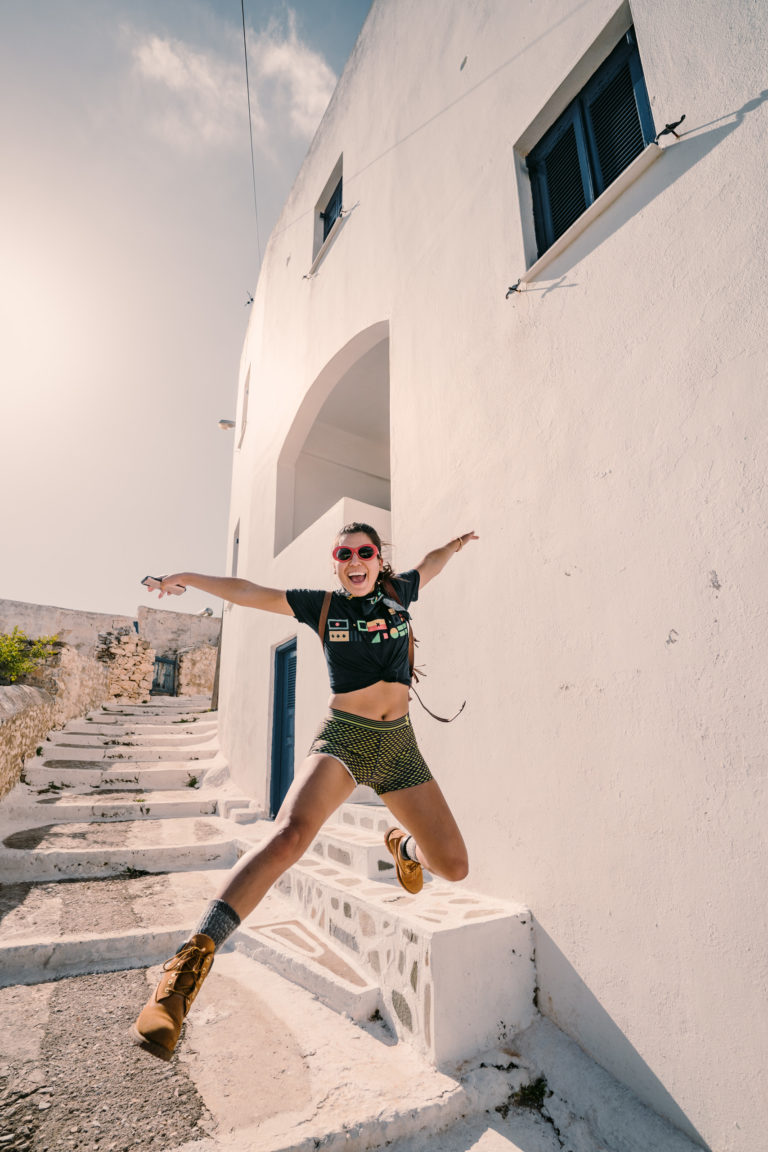 An asian woman jumps in the air on the streets of Greece.