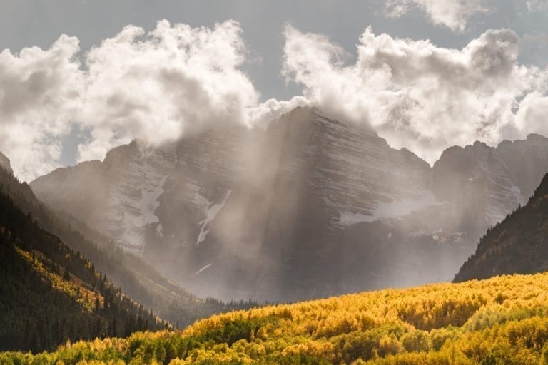 Sun rays coming through clouds above Maroon Bells, with changing Aspen trees near Aspen Colorado.