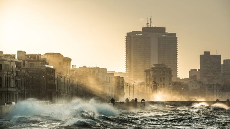 Water splashes over the Malecón in Havana, Cuba, during sunset.