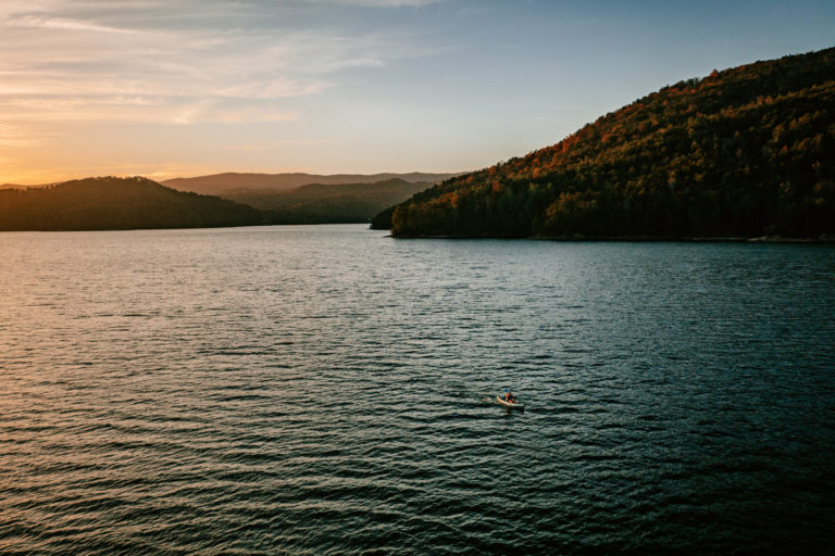 A kayaker paddles across the open water on Lake Jocassee at sunset.