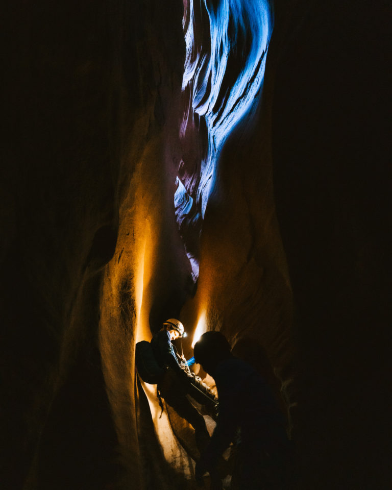 A climber descends a very dark slot canyon using a headlight.