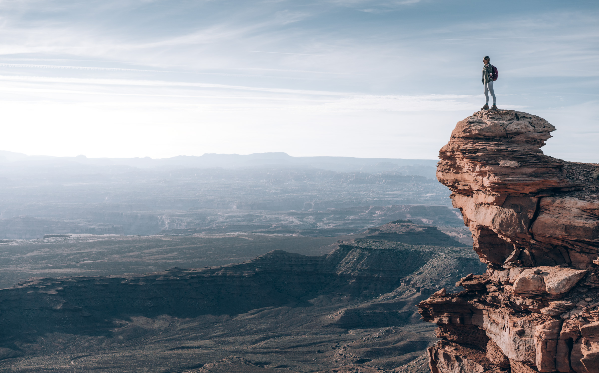 An athletic woman stands atop a very sheer dropoff at Island in the Sky, Canyonlands National Park