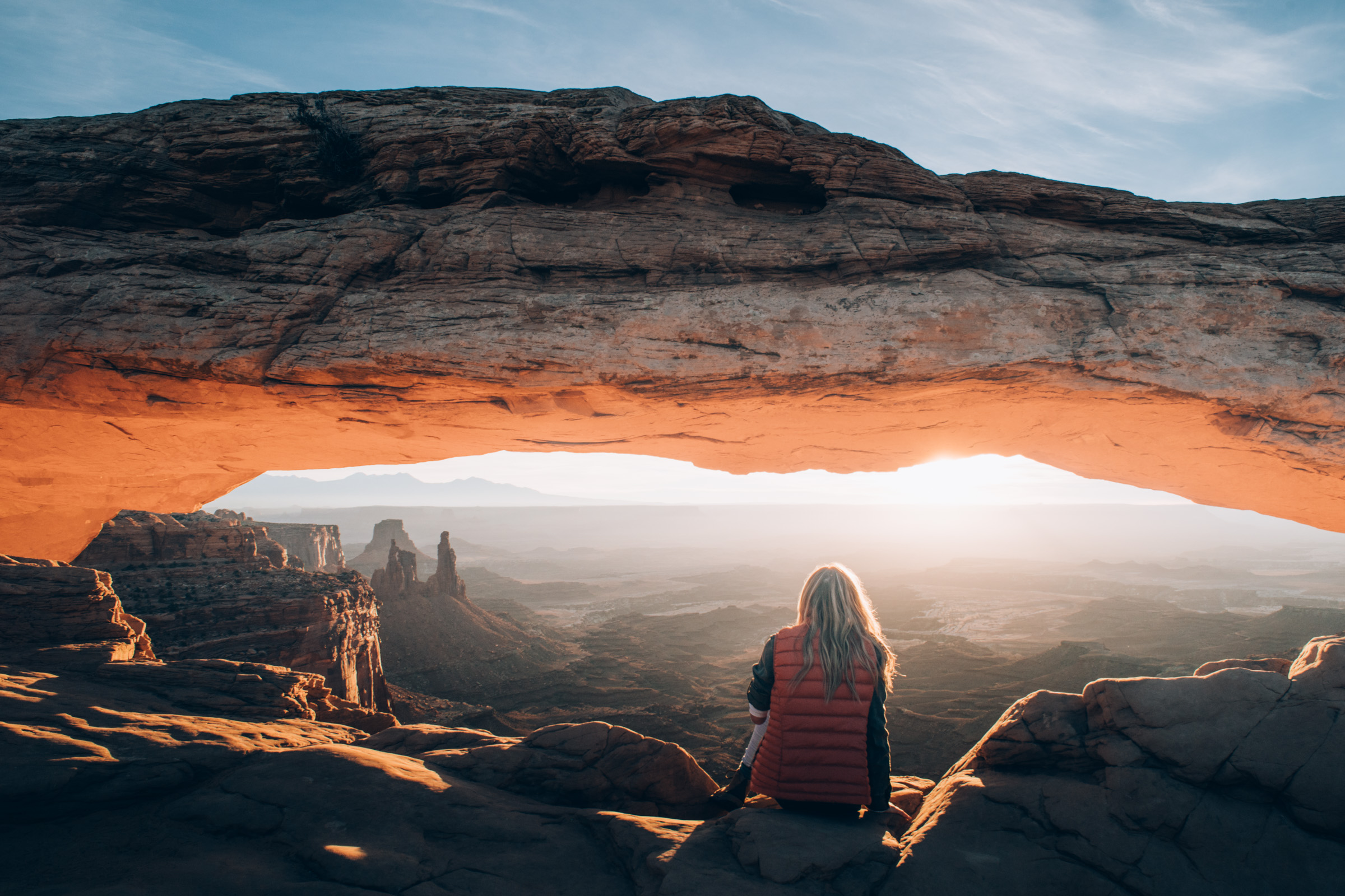 A woman watches the sunrise under Mesa Arch at Canyonlands National Park, Utah