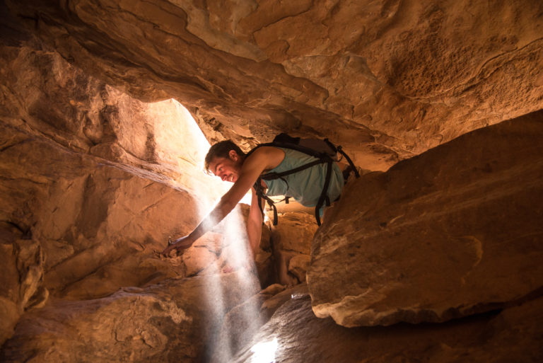 A man climbs through a shaft of light in Canyonlands National Park