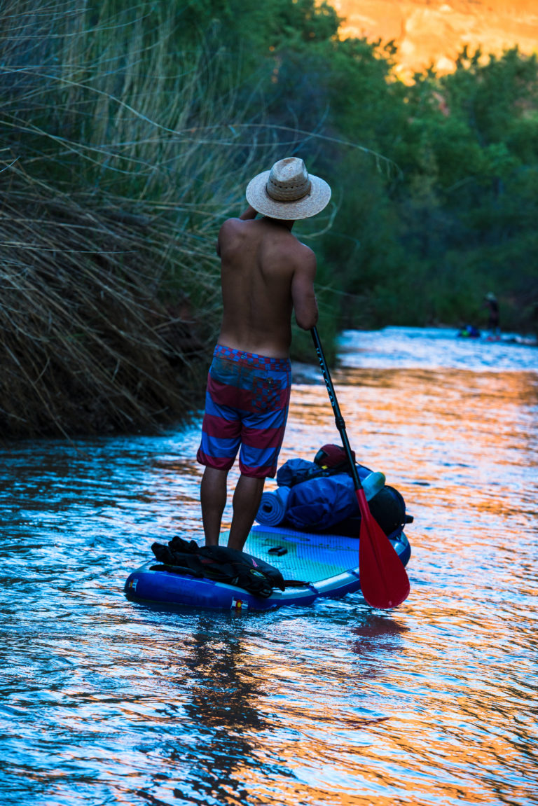 A standup paddleboarder descends the Escalante River, Utah, during sunset.
