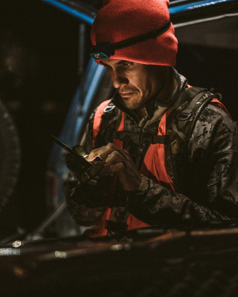 A hunter looks at his phone while sitting on his tailgate at night