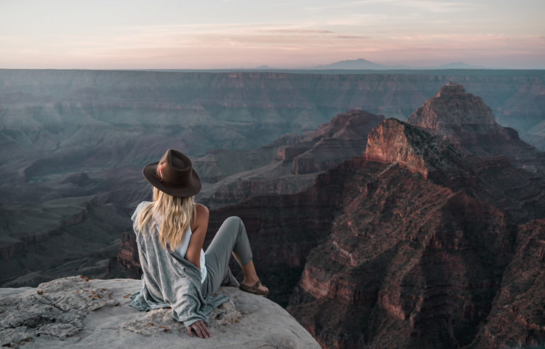 A woman in a hat looks over the Grand Canyon at sunrise