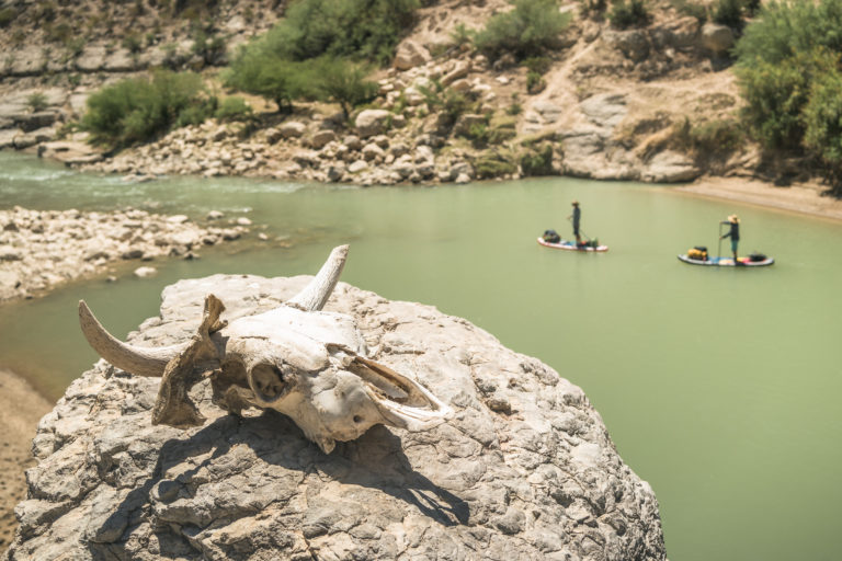 People paddle past a skull on the rio grande river