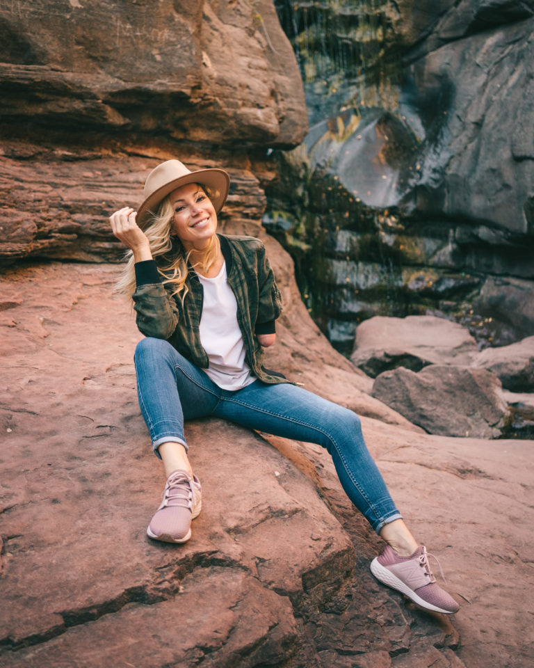 Beautiful woman sits near waterfall in trendy outfit.