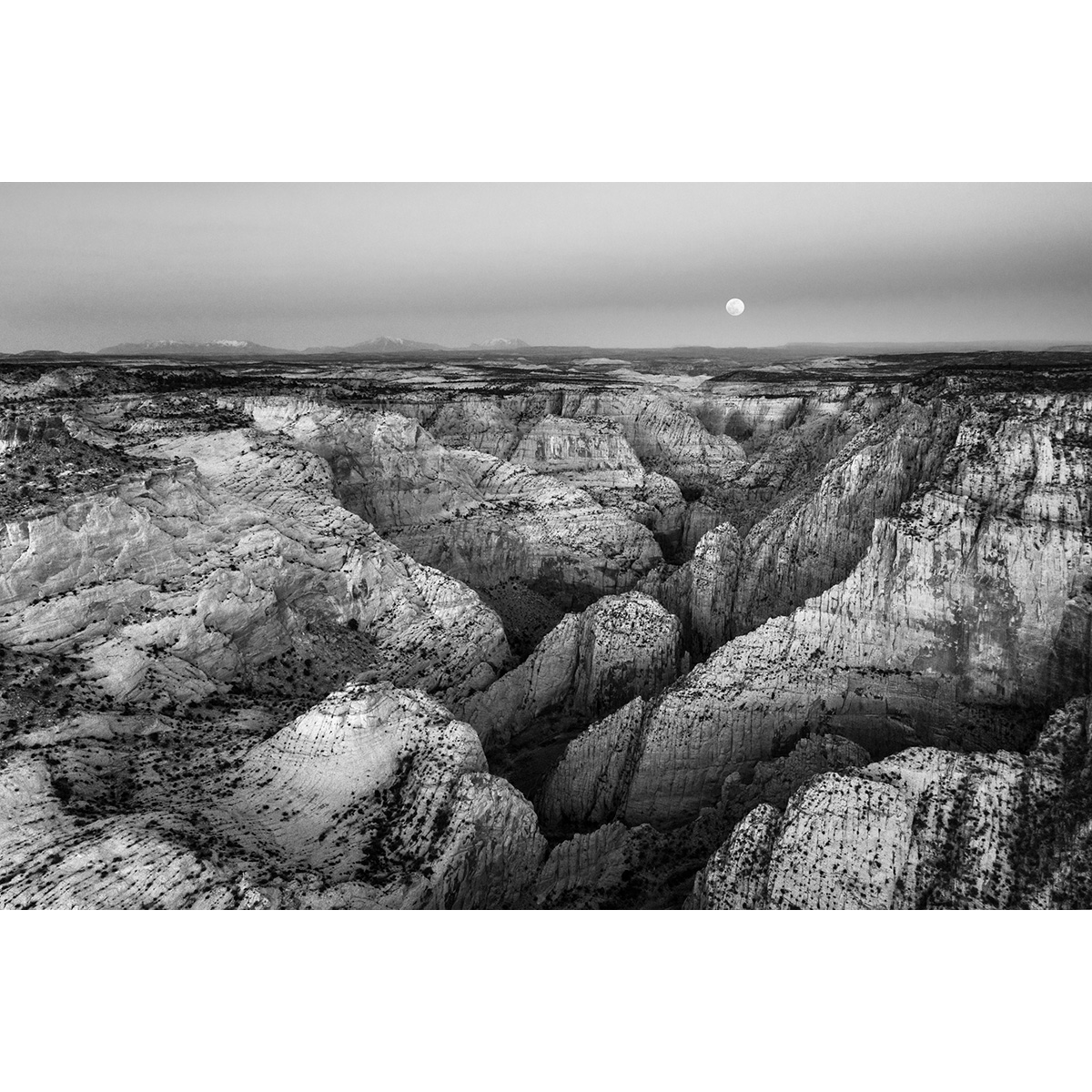 A black and white fine-art photograph of a full moon rising over the Escalante drainage.