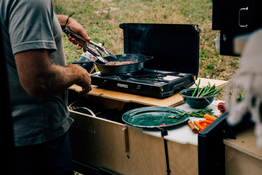A man cooks outside of a camping trailer.